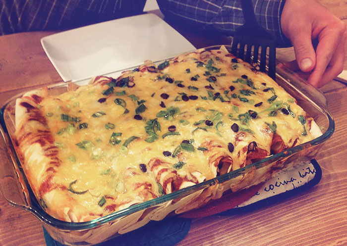 A 9x13 glass dish with enchiladas covered in sauce and melted cheese, topped with chopped green onions and black beans.