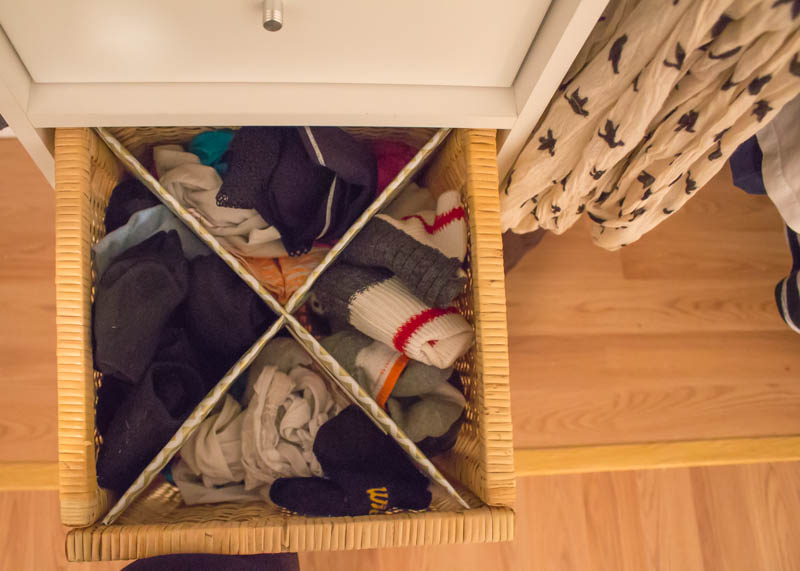 A wooden basket pulled out from the shelf with an 'X' shaped divider. The for sections are filled with socks, ankle socks, and under garments.